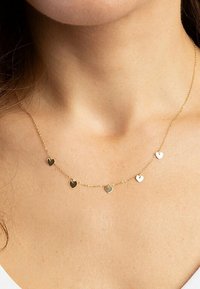 Gold chain necklace featuring five small heart-shaped pendants, alternating in polished and matte finishes, resting near the collarbone.