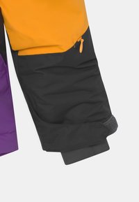 Rukáv izolované bundy v oranžové, černé a fialové barvě, vybavený kapsou na zip a nastavitelným manžetovým zakončením se suchým zipem.