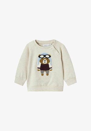 Felpa color beige chiaro con un design di un orso pilota, dotato di un cappellino blu e occhiali. Polsini e orlo inferiore a costine, dettagli in ricamo testurizzato.