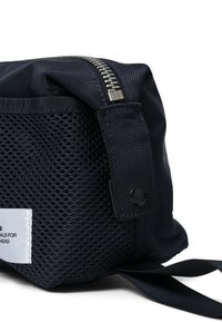 Mustapohjainen nylontasku, jossa on teksturoitu verkko-paneeli, hopeinen vetoketju ja olkahihna. Mukana on valkoinen etiketti, jossa on painettua tekstiä.