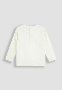Hosszú ujjú, off-white (krémszínű) babaing, három patentgombbal a hátsó gallérnál, szürke háttéren.