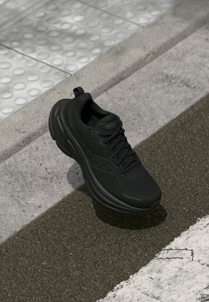Schwarzer Sportschuh mit strukturiertem Mesh-Obermaterial, dicker Sohle und Schnürsenkeln. Verfügt über ein kleines Logo und eine Zuglasche an der Ferse.