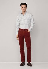 Herroutfit med en vit rutig skjorta med knappar och röda manchesterbyxor, kompletterat med bruna läderstövlar.