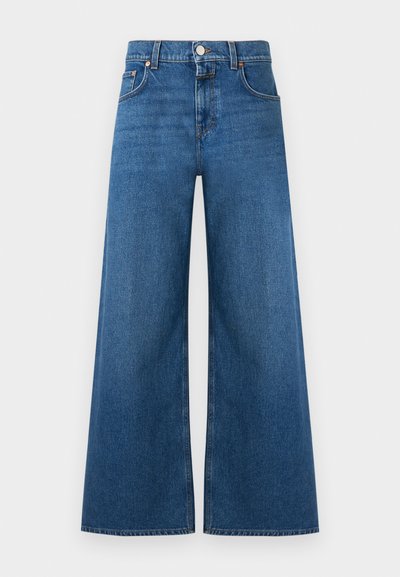 Jean en denim à jambes larges de couleur bleu moyen, fabriqué en tissu de coton résistant. Il présente une taille boutonnée, cinq poches et des ourlets droits.