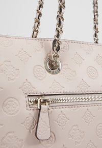 Ljusrosa handväska i präglat läder med en dragkedjeficka. Har en kedjerem och metalldetalj med logga. Mönster med texturerade blommor.