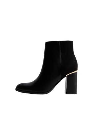 Schwarzer Leder- und Wildleder-Stiefelette mit spitzer Schuhspitze, Blockabsatz und goldenem Akzent in der Nähe der Ferse auf weißem Hintergrund.