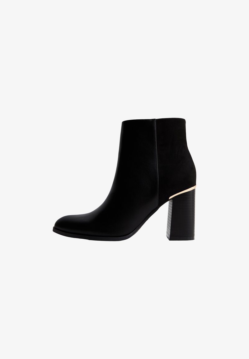 Bottine noire en cuir et suède avec bout pointu, talon bloc et accent doré près du talon sur fond blanc.