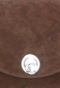 Borsa in suede marrone con chiusura rotonda in argento, texture liscia, pattina curva e cuciture ordinate lungo il bordo.