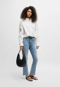 White shirt with tie-detail sleeves, light blue flared jeans, black sandals, and a black hobo bag. Flat texture, casual design, modern look.