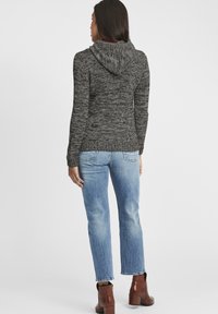 Grå stickad cardigan med huva, med ett strukturerat mönster, i kombination med ljusblå raka jeans och bruna ankelskor.