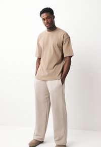 Beežist puuvillast lühikeste käistega t-särk, kombineeritud lahtiste beežide pükstega ja pehmete beežide sussidega. Minimalistlik ja vabaaja stiil.