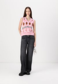 Strikket rosa vest med pepperkake- og snømannmønster, kombinert med vide svarte jeans og klumpete svarte sko. Akkompagnert med en hvit veske.