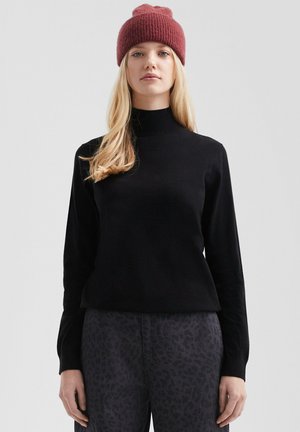 Black turtleneck sweater in soft material, paired with dark gray leopard print pants. The model wears a burgundy ribbed beanie.
