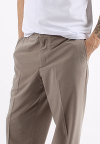 Pantaloni beige con una texture liscia, design a gamba dritta e tasche laterali. Indossati con una t-shirt bianca casual.