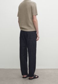 Lyhythihainen, beige poolopaita, jossa on teksturoitu kangas, yhdistetty tummansinisiin farkkuihin. Malli pukeutunut mustiin sandaaleihin. Takakuvassa.