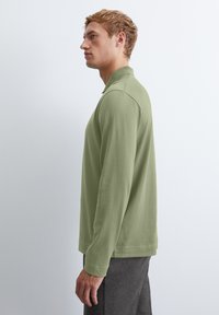 Langärmliges Poloshirt aus weichem grünen Baumwollstoff. Mit klassischem Kragen, gerippten Bündchen und geradem Saum. Minimalistisches Design und glatte Textur.