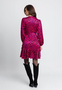 Różowa sukienka w wzór houndstooth, dopasowana góra, bufiaste rękawy, falbaniasty dół i pasujący pasek. Założona z czarnymi kozakami do kolan.