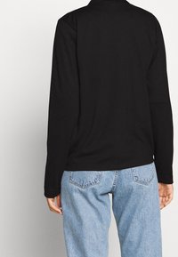 Svart långärmad topp med en slät yta, med krage och en något lös passform, som matchas med ljusblå denimbyxor.