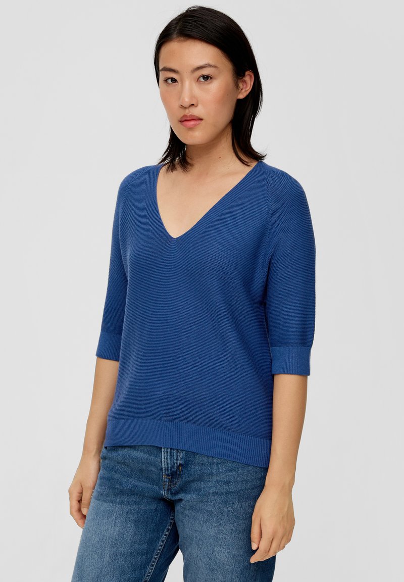 Blauer Strickpullover mit V-Ausschnitt und kurzen, gerippten Ärmeln. Der Stoff ist strukturiert mit einer taillierten Passform und einem Saum, der auf der Taille sitzt.