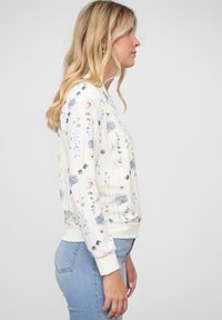 Sweatshirt floral en crème avec des motifs de fleurs bleues et roses. Présente un col rond, des poignets et un ourlet côtelés. Assorti avec un jean bleu clair.