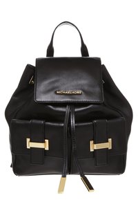 Zaino in pelle nera con pattina superiore, hardware dorato prominente, due tasche frontali e chiusura con cordoncino. Finitura testurizzata con branding.