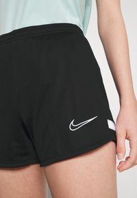 Shorts deportivos negros con cintura elástica, con un logo de Nike blanco y una pequeña abertura lateral. Tejido suave y ligero.