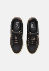 Black sneakers with a smooth leather upper, featuring snake print accents, contrasting yellow sole, and metal eyelets for laces.