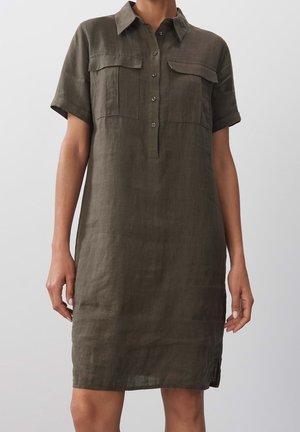 Robe chemise en lin vert olive avec des manches courtes, un col, deux poches avant et une patte de boutonnage, présentant une coupe décontractée et des fentes sur les côtés.