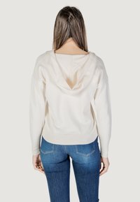 Felpa color crema con una texture morbida, presenta un collo a V e polsini a costine. Abbinata a jeans blu slim.
