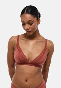 Soutien-gorge de couleur rouille en tissu doux et lisse. Il présente un décolleté plongeant, des finitions en dentelle délicate sur les bords, et des bretelles ajustables.