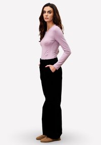 Un haut long à manches lavande claire associé à un pantalon en velours côtelé noir taille haute. L'ensemble présente des manches ajustées et des poches latérales.