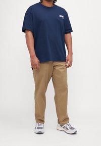 Tmavě modré bavlněné tričko s bílým nápisem "NYC", doplněné khaki chinos kalhotami a šedo-bílými teniskami s vlnitým vzorem.