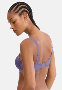 Μωβ σουτιέν με ρυθμιζόμενες ράντες, υφή υφάσματος και κλείσιμο με αγκράφα στην πλάτη. Ομαλή επιφάνεια χωρίς επιπλέον διακοσμητικά.