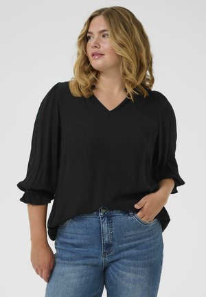 Zwarte V-hals blouse met gepofte mouwen, gemaakt van gestructureerde stof. Gepaard met blauwe denim jeans. Geen zichtbare patronen of accenten.