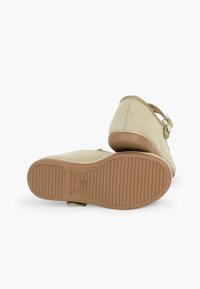 Beige Wildlederschuhe mit rundem Zehenbereich, verstellbarem Riemen und Gummisohle mit einem strukturierten Grippmuster.
