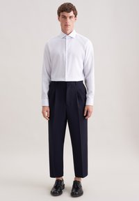 Weiß kariertes Hemd mit Knöpfen, dunkle plissierte Hose und schwarze Lederschuhe. Das Hemd hat lange Ärmel und einen spitzen Kragen.