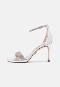 Sandale à talons hauts en argent métallique avec une finition brillante, dotée d'une bande d'accent en strass et d'une bride de cheville avec une fermeture à boucle.