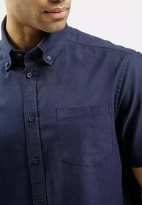 Granatowa koszula z krótkim rękawem wykonana z bawełnianej tkaniny, z kołnierzykiem zapinanym na guziki, przednią kieszenią oraz widocznymi guzikami wzdłuż listwy.