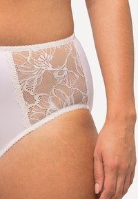Witte hoog uitgesneden slip met een kant- en gaas zijpaneel, versierd met bloemmotieven en gerafelde rand langs de tailleband.