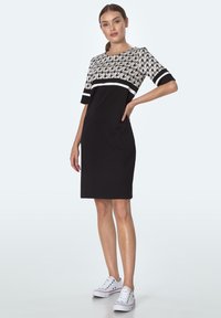 Czarna krótka sukienka z góry w wzór w szachownicę, białym akcentującym paskiem i krótkimi rękawami. Zestawiona z białymi trampkami. Gładka faktura materiału.