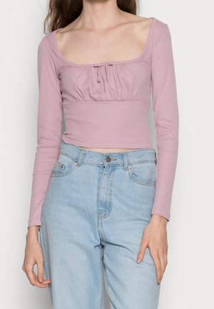 Vrouw draagt een lichtpaarse geribbelde crop top met lange mouwen en een vierkante halslijn, gecombineerd met lichtblauwe, hoogwater jeans.