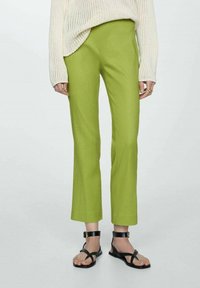 Groene rechte broek van lichtgewicht stof, gecombineerd met een crèmekleurige gebreide trui en zwarte sandaaltjes met bandjes. Voorpaneel ontwerp.