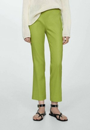 Grüne gerade geschnittene Hose aus leichtem Stoff, kombiniert mit einem cremefarbenen Strickpullover und schwarzen Riemchensandalen. Flacher Vorderteil.