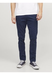 Pantalones de algodón azul marino con un ajuste slim. Diseño sencillo, con bolsillos frontales y presillas para cinturón. Se combinan con zapatillas deportivas blancas.