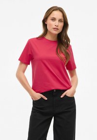 Dopasowany t-shirt z krótkim rękawem w jasnoróżowej bawełnie z okrągłym dekoltem, zestawiony z czarnymi, spodniami z wysokim stanem. Gładka tekstura, casualowy design.