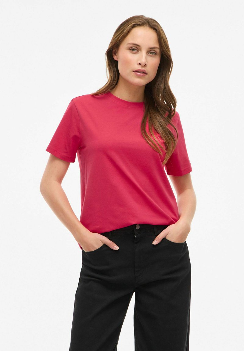 Dopasowany t-shirt z krótkim rękawem w jasnoróżowej bawełnie z okrągłym dekoltem, zestawiony z czarnymi, spodniami z wysokim stanem. Gładka tekstura, casualowy design.