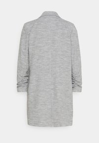 Grå kavaj med ett texturerat tyg, som har krage, trekvartslånga ärmar och rynkdetaljer på ärmarna.