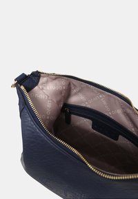 Interno della borsa in pelle blu navy con una tasca con zip e foderato in tessuto liscio caratterizzato da un motivo di logo ripetitivo in beige.