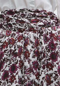 Bloemrijke rok met een gesmokte tailleband. Heeft een witte achtergrond met rode, paarse en zwarte bloemenpatronen; textuurstof.