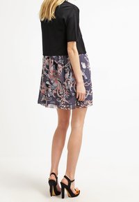 Svart croppad topp matchad med en klänning med blommönster i marinblå och rosa nyanser. Svarta högklackade sandaler med orange detaljer fulländar looken.